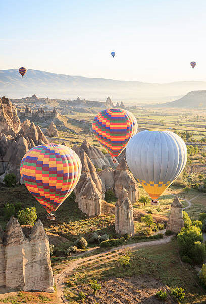 "Hot air ballons over Love Valley near Goreme and Nevsehir in the center of Cappadocia, Turkey (region of Anatolia). This shot taken shortly after sunrise.Three million years ago the nearby volcano Erciyes spit out ashes to form a layer of tuff. In some places these are covered by a layer of basalt lava. Then the more durable basalt cracked and split under attack from the weather. Rainwater washed out the cracks and eroded the tuff. In a lot of areas this resulted in these cone formed rocks with a hard basalt top. The Turks call them Fairy Chimneys.Goreme National Park is a UNESCO World Heritage Site.See also"