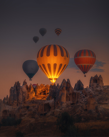 Spectacular sunset landscape view of hot air balloon illuminated with fire in sky tour over amazing fairy chimneys rock forms on valleys and fields in early morning in Kapadokya, Göreme National Park, Turkiye. Dreamy nature background.